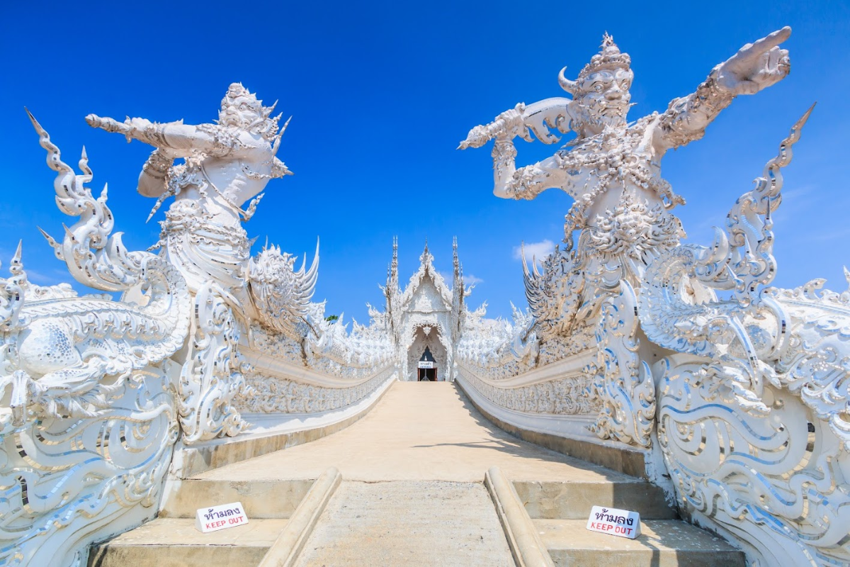 Gleaming white facade of Wat Rong Khun under blue skies